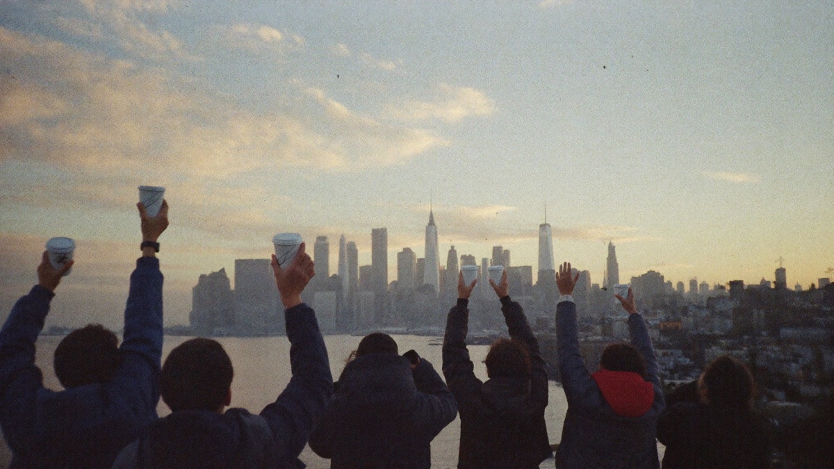 People on a rooftop at dawn raising paper coffee cups toward the Manhattan skyline